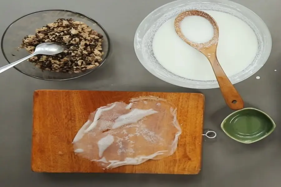 Bánh cuốn được đặt trên mặt thớt, có tô thịt góc 11h và tô đựng bột ở góc 1h