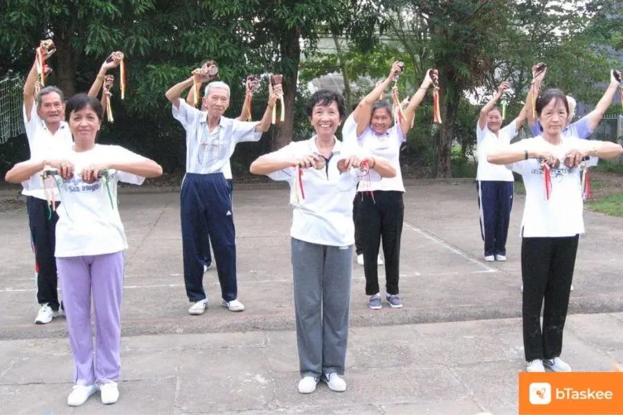 Các cụ bà, cụ ông mặc đồ trắng, đứng xếp hàng ngay ngắn khởi động tập dưỡng sinh